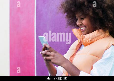 Bonne fille en utilisant un smartphone debout près d'un mur coloré Banque D'Images