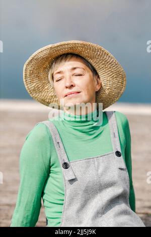 Femme mature portant un chapeau assis avec les yeux fermés le jour ensoleillé Banque D'Images