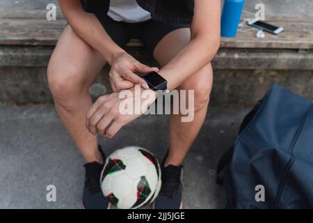 Femme avec ballon de football vérifiant le temps dans la montre intelligente Banque D'Images