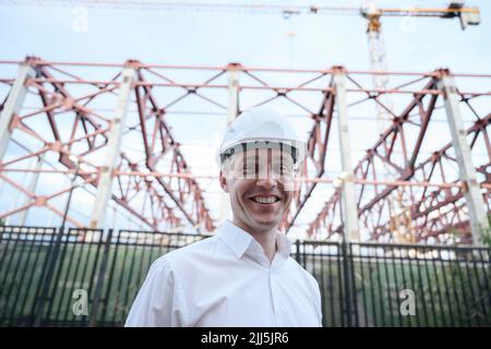 Un ingénieur heureux portant un casque de sécurité debout devant le cadre de construction Banque D'Images