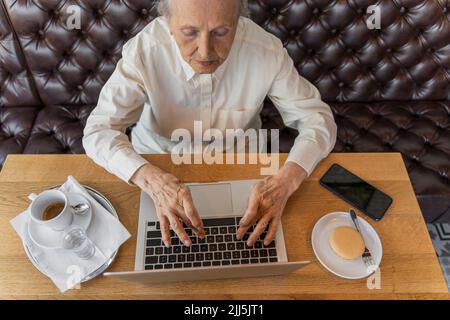 Femme âgée travaillant sur un ordinateur portable dans un café Banque D'Images