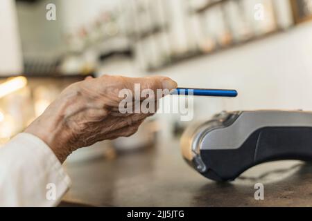 Main d'une femme âgée qui paie par téléphone intelligent au café Banque D'Images