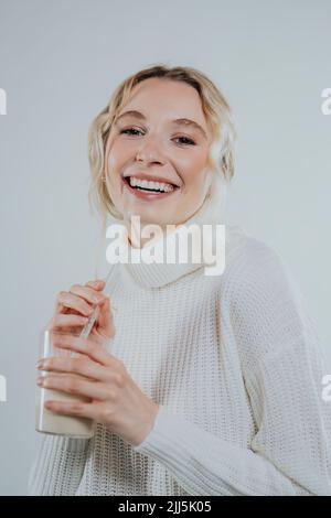 Jeune femme souriante dans le col de cygne tenant un verre de lait végétal sur fond blanc Banque D'Images