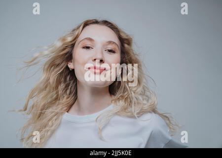 Jeune femme aux cheveux blonds souriant sur fond gris Banque D'Images