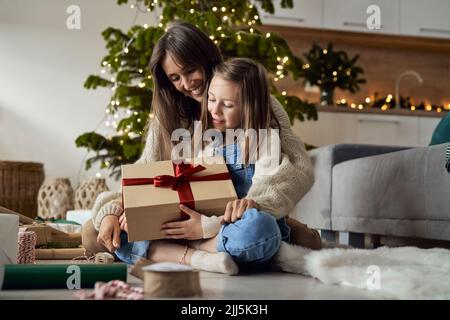 Fille tenant un cadeau de Noël assis avec une mère sur le sol à la maison Banque D'Images