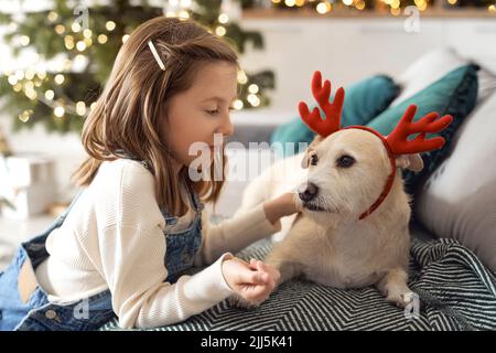 Fille regardant un chien portant une garde assise sur un canapé à la maison Banque D'Images