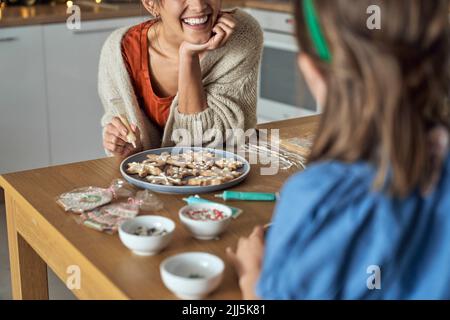 Bonne mère avec sa fille décorant un biscuit au pain d'épice dans la cuisine Banque D'Images