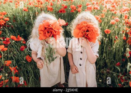 Fille avec soeur cachant le visage avec fleur dans champ de pavot Banque D'Images