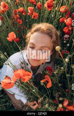 Femme avec les yeux fermés assis au milieu de fleurs rouges dans le champ Banque D'Images