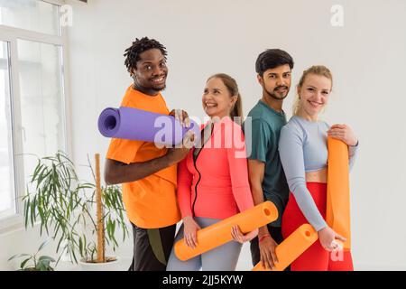 Heureux amis multiraciaux tenant des tapis d'exercice dans le studio de yoga Banque D'Images