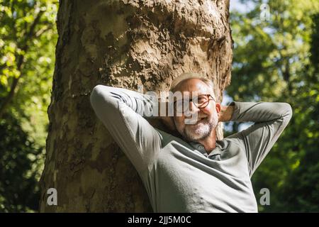 Homme heureux avec les mains derrière la tête penchées sur le tronc de l'arbre Banque D'Images