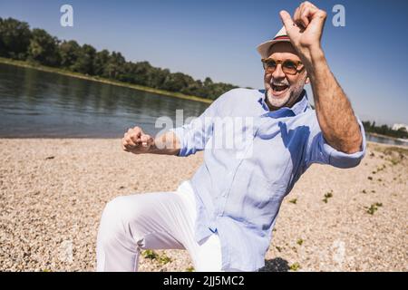 Un homme senior heureux dansant au bord de la rivière par beau temps Banque D'Images