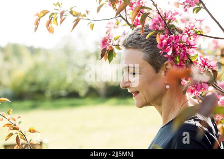 Femme souriante debout près d'une branche de fleurs roses dans le jardin Banque D'Images