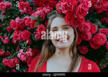Femme souriante aux cheveux bruns au milieu de la rose rouge Banque D'Images