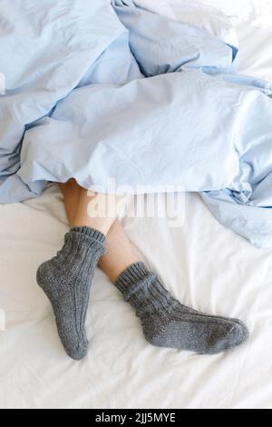 Jambes de femme portant des chaussettes confortables sous une couverture sur le lit Banque D'Images