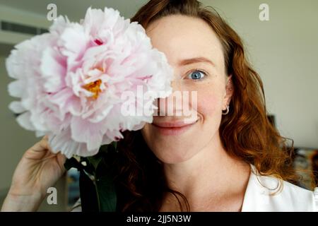 Femme souriante tenant la fleur devant les yeux Banque D'Images