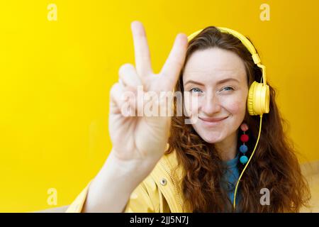 Femme souriante portant un casque gestante signe de paix devant le mur jaune Banque D'Images
