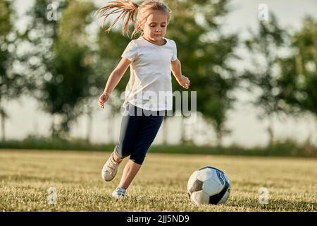 Blonde fille jouant au football sur le terrain de sport le jour ensoleillé Banque D'Images