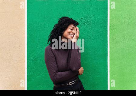 Femme souriante couvrant l'œil debout devant le mur vert Banque D'Images