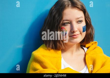 Adolescente, avec un symbole de paix et de la peinture de l'Union européenne sur les joues devant le mur bleu Banque D'Images