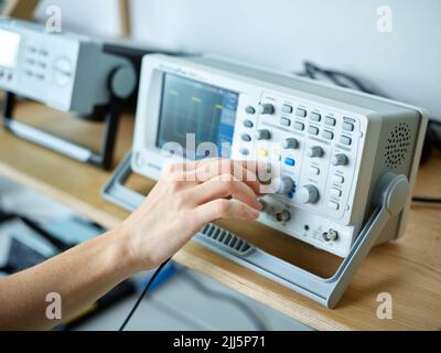 Main de l'ingénieur pour régler l'oscilloscope dans un laboratoire électronique Banque D'Images