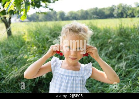 Jolie fille souriante portant des boucles d'oreilles en cerisier sur le terrain Banque D'Images
