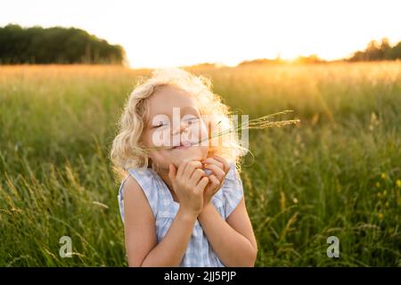 Fille blonde souriante avec herbe dans la bouche en appréciant sur le terrain Banque D'Images