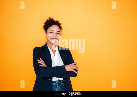 Jeune femme souriante avec bras croisés debout sur fond jaune Banque D'Images