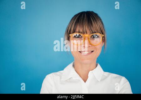Femme d'affaires souriante portant des lunettes sur fond bleu Banque D'Images