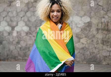 Femme souriante couverte d'un drapeau arc-en-ciel devant le mur Banque D'Images