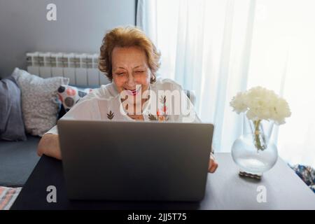 Femme âgée souriante utilisant un ordinateur portable à la maison Banque D'Images