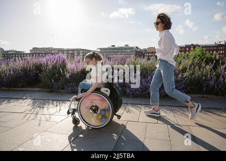 Mère en train de courir après une fille handicapée en fauteuil roulant au parc Banque D'Images