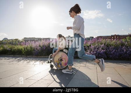 Mère en train de courir après la fille en fauteuil roulant au parc Banque D'Images