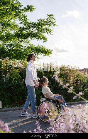 Femme poussant la fille handicapée assise en fauteuil roulant au parc Banque D'Images