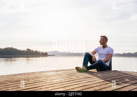 Homme mature assis sur la jetée au lac Banque D'Images
