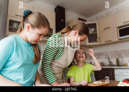 Une fille heureuse avec sa mère et sa sœur préparant la nourriture dans la cuisine à la maison Banque D'Images