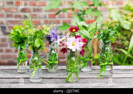 Herbes fraîches et fleurs dans des bouteilles de verre décorées sur une table de balcon Banque D'Images