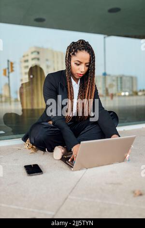 Jeune femme d'affaires utilisant un ordinateur portable devant un mur de verre Banque D'Images
