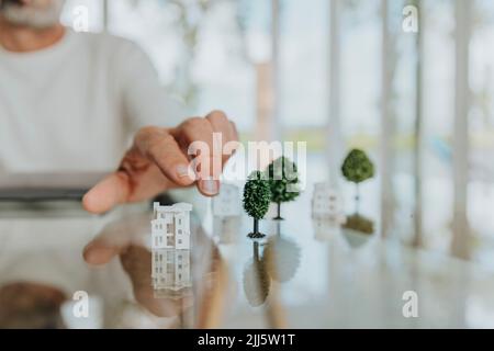 Homme avec maison modèle et arbres sur table à la maison Banque D'Images