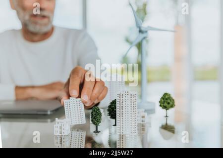 Homme mature touchant la maison modèle par l'éolienne sur la table Banque D'Images