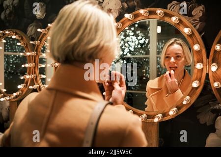 Belle femme appliquant le rouge à lèvres regardant dans le miroir Banque D'Images