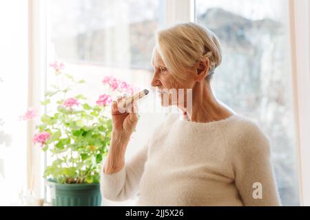 Femme âgée qui sent palo santo Stick à la maison Banque D'Images