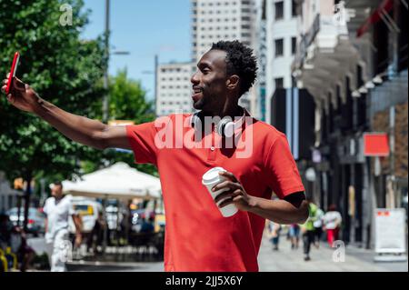 Homme tenant une tasse de café prenant le selfie en ville le jour ensoleillé Banque D'Images