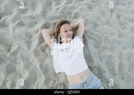 Femme souriante avec les mains derrière la tête, allongé sur la plage Banque D'Images