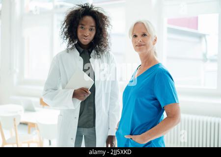 Infirmière avec les mains dans les poches debout par une femme médecin tenant un PC tablette Banque D'Images