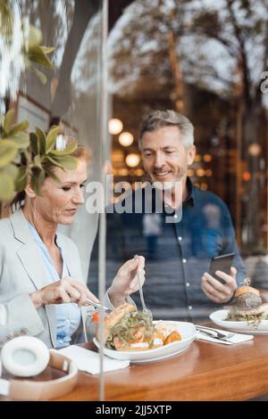 Femme d'affaires avec un homme d'affaires tenant un téléphone mobile prenant le déjeuner dans un café Banque D'Images