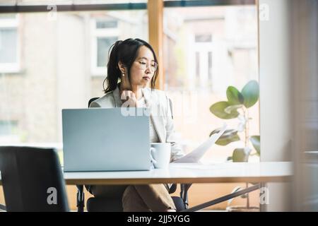 Femme d'affaires avec lunettes lisant le document au bureau Banque D'Images