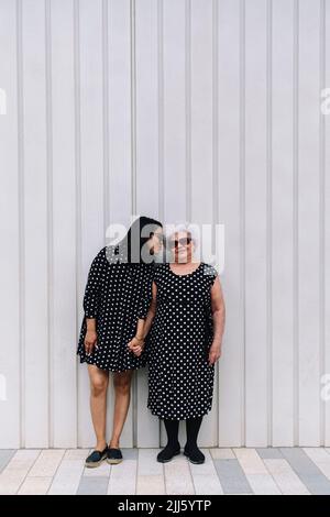 Femme embrassant mère sénior debout devant le mur Banque D'Images