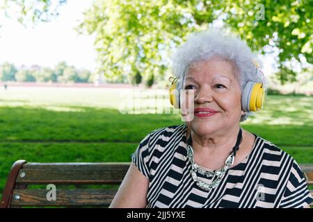 Bonne femme âgée avec un casque sans fil qui écoute de la musique au parc Banque D'Images