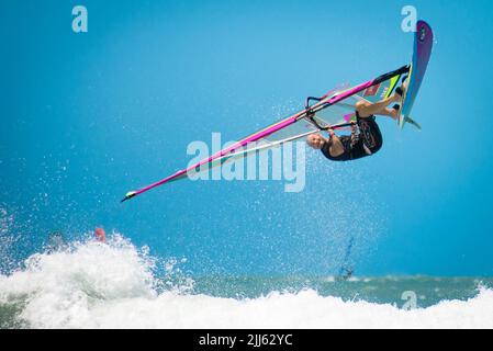 Une planche à voile au milieu du saut a un ciel bleu avec du surf blanc au premier plan Banque D'Images